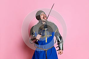 Portrait of man, medieval warrior or knight in armor with sword isolated over pink studio background