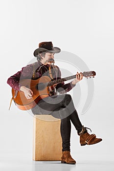 Portrait of man with moustaches in country cowboy style clothes playing guitar and harmonica, performing  over