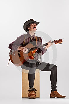 Portrait of man with moustaches in country style clothes playing guitar, singing isolated over white background