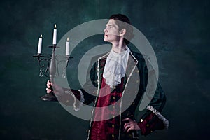 Portrait of man in noble medieval costume in image of vampire holding candles  over dark green background