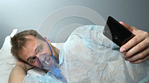 portrait of man in oxygen mask using phone while lying on bed in hospital