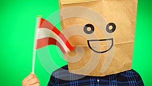 Portrait of man with paper bag on head waving Austrian flag with smiling face against green background.