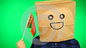 Portrait of man with paper bag on head waving Belarusian flag with smiling face against green background.