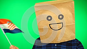 Portrait of man with paper bag on head waving Croatian flag with smiling face against green background.