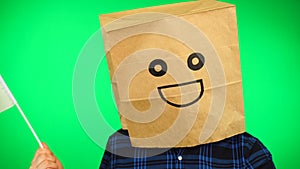 Portrait of man with paper bag on head waving Cypriot flag with smiling face against green background.