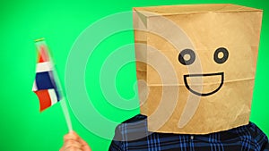 Portrait of man with paper bag on head waving Dominican Republic flag with smiling face against green background.