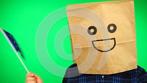 Portrait of man with paper bag on head waving European flag with smiling face against green background.