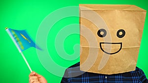 Portrait of man with paper bag on head waving Kazakhstan flag with smiling face against green background.