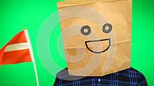 Portrait of man with paper bag on head waving Latvian flag with smiling face against green background.