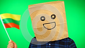 Portrait of man with paper bag on head waving Lithuanian flag with smiling face against green background.