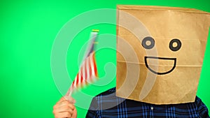 Portrait of man with paper bag on head waving Malaysian flag with smiling face against green background.