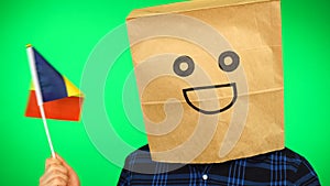 Portrait of man with paper bag on head waving Moldavian flag with smiling face against green background.