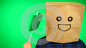 Portrait of man with paper bag on head waving Turkmenistan flag with smiling face against green background.