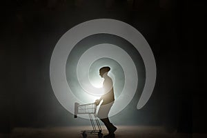 Portrait of a man pushing an empty shopping cart isolated on black background