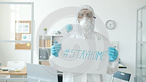 Portrait of man in quarantine suit standing in empty office with stayhome banner