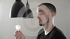 Portrait of man replacing the old incandescent bulb with a new energy efficient LED bulb in lamp. Screwing energy saving bulb