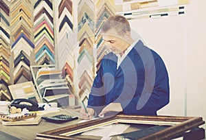 Portrait of man seller working with picture frames in atelier