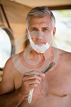 Portrait of man shaving his beard with razor in cottage