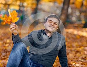 Portrait of a man, he is sitting in a glade with yellow maple leaves, closed his eyes and dreams, a bright sunny day in an autumn