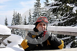 Portrait of man in ski clothes, with ski goggles on his head, sits at table outdoors. skier is resting after skiing, smiling,