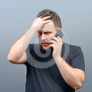 Portrait of a man slapping his forehead while talking on cellphone against gray background