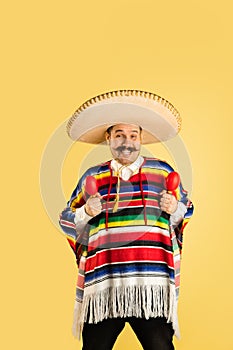 Portrait of man in sombrero and bright poncho isolated over yellow background