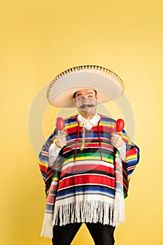 Portrait of man in sombrero and bright poncho isolated over yellow background