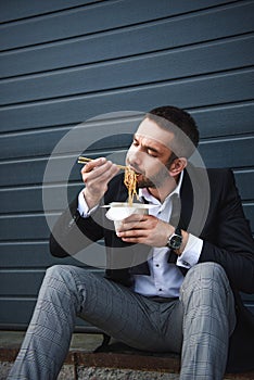 portrait of man in stylish suit with chopsticks eating asian food photo