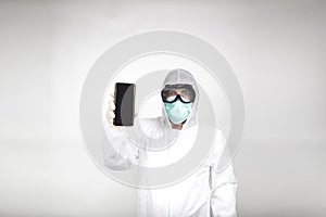 Portrait of man in surgical mask wearing white protective suit with mobile phone isolated in studio on white background.