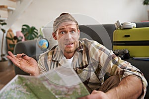 Portrait of man, tourist looking confused at travel map, shrugging, cant decide on route, choosing the road for