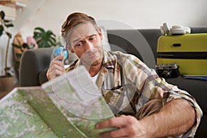 Portrait of man, tourist looking confused at travel map, shrugging, cant decide on route, choosing the road for