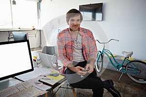 Portrait of man using phone while sitting on desk at office