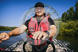 portrait of a man on vacation in nature, riding an airboat on the river in hunter's clothes