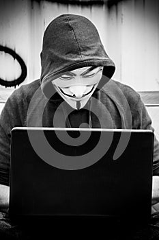 Portrait of man with Vendetta mask and coumputer in abandoned factory on vintage armchair