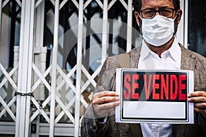 Portrait of man wear medical mask for coronavirus economy crisis with closed business and se vende spanish panel - concept of photo