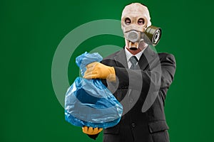 Portrait of a man wearing a dark business suit and a gas mask holding a blue garbage bag, isolated on green background