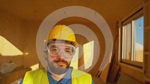 PORTRAIT Man wearing hard hat and safety goggles stands in a modern wooden house