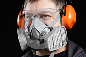 Portrait of a man wearing a respirator and protective noise-cancelling headphones earmuffs