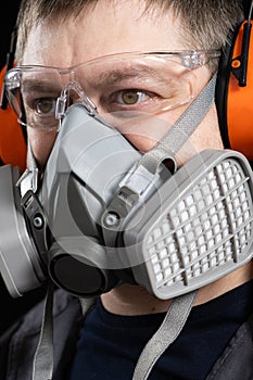 Portrait of a man wearing a respirator and protective noise-cancelling headphones earmuffs