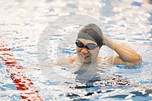 Asian man in hat and goggles swimming in indoors swimming pool photo