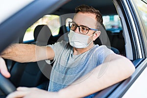 Portrait of man wearing surgical mask while driving a car