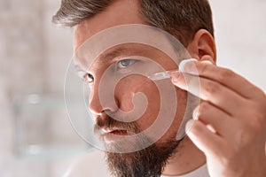 Portrait of man in white tshirt applying serum on his face at bathroom. Self care morning procedure