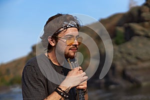 portrait of a man who sits leaning on a ukulele in nature by the lake