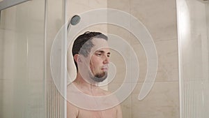 Portrait of man who stands with a serious view under the shower in the bathroom