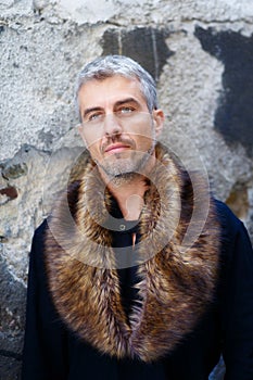 Portrait of a man in wolf fur and thoughtful expression on his face, a structure wall on background