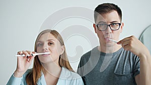 Portrait of man and woman brushing teeth smiling looking at camera at home