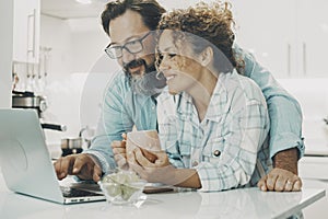 Portrait of man and woman at home enjoyng surf the web together with wireless laptop. White modern kitchen apartment in background