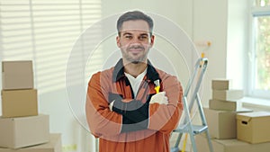 Portrait of the man worker standing, folding his arms, holding paintbrush in new apartment renovation room. Craftsman in