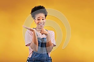 Portrait, marketing and a black woman pointing to her palm for the promotion of a product on a yellow background in