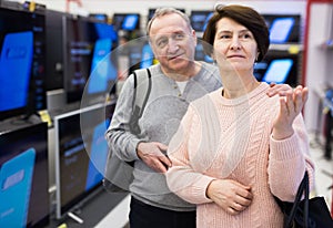 Portrait of a of mature age couple standing in the department with televisions